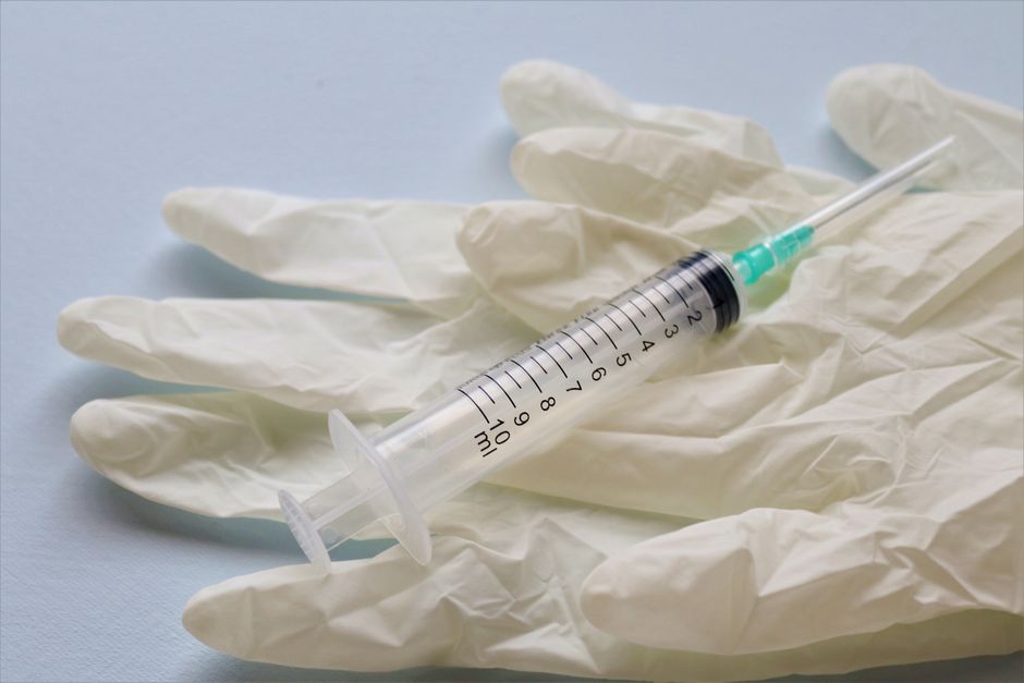Close-up of a syringe and medical gloves on a flat surface, showcasing healthcare tools.