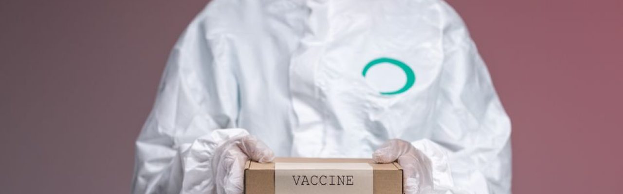 Medical worker in protective uniform holding a vaccine box in a studio setting.